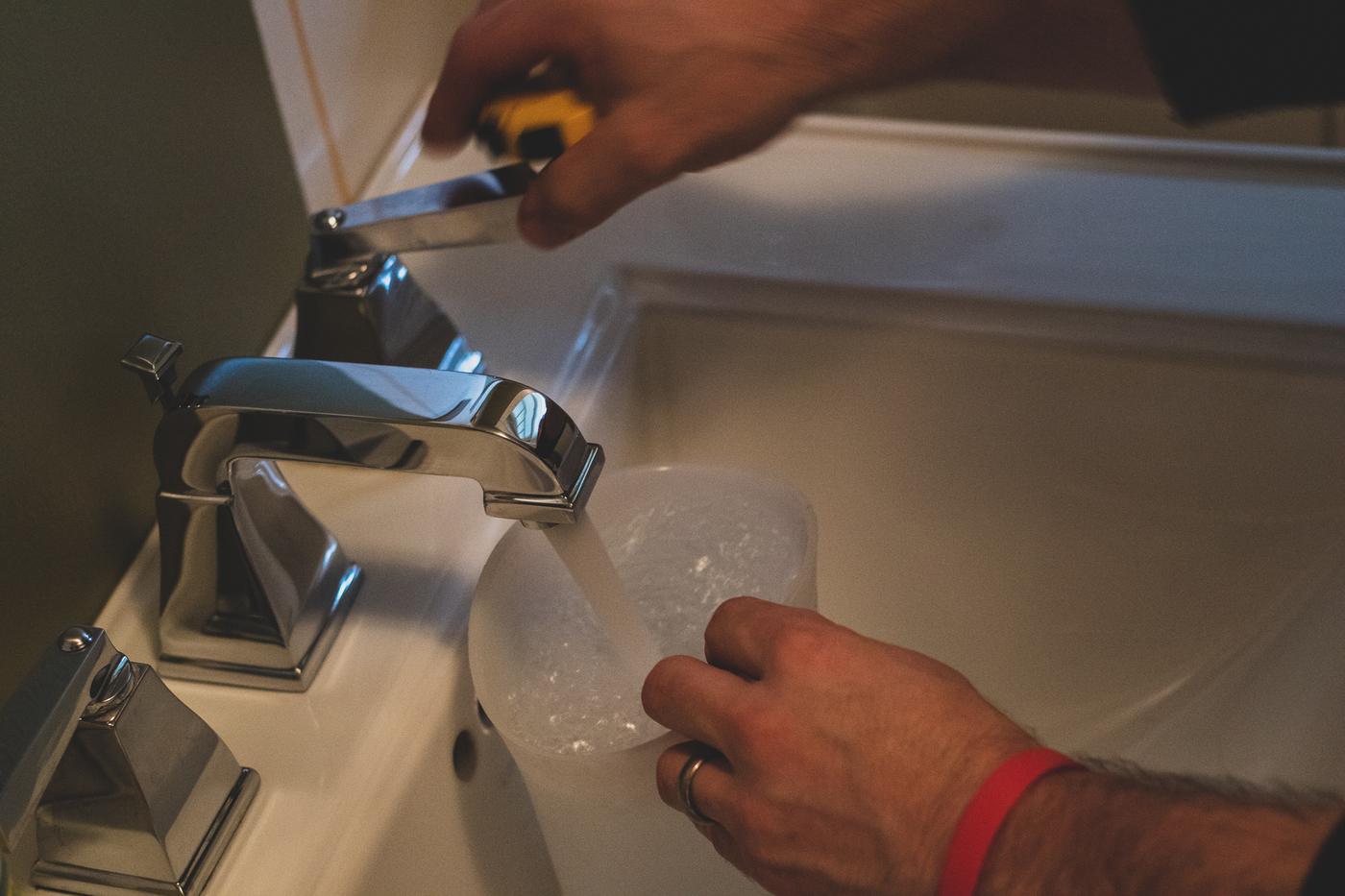 A technician measures a bathroom faucet’s flow with a measuring cup