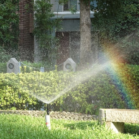 A pop-up sprinkler spraying over a lawn, with a rainbow in the mist