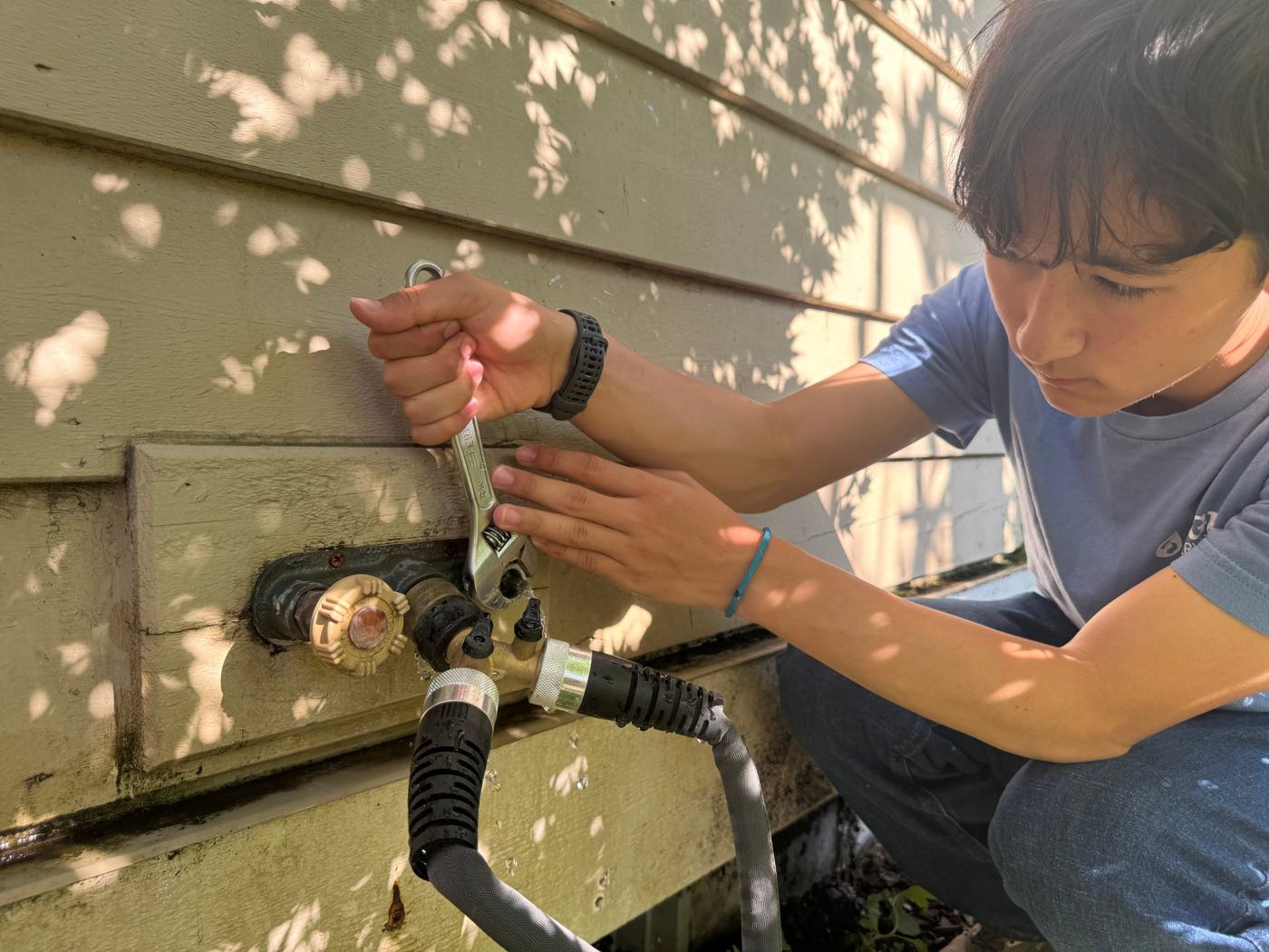 Rylan tightens an outdoor spigot fitting with a wrench