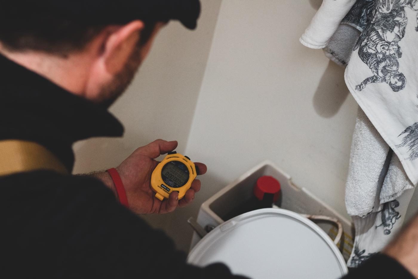 A technician times a toilet tank refill with a yellow stopwatch